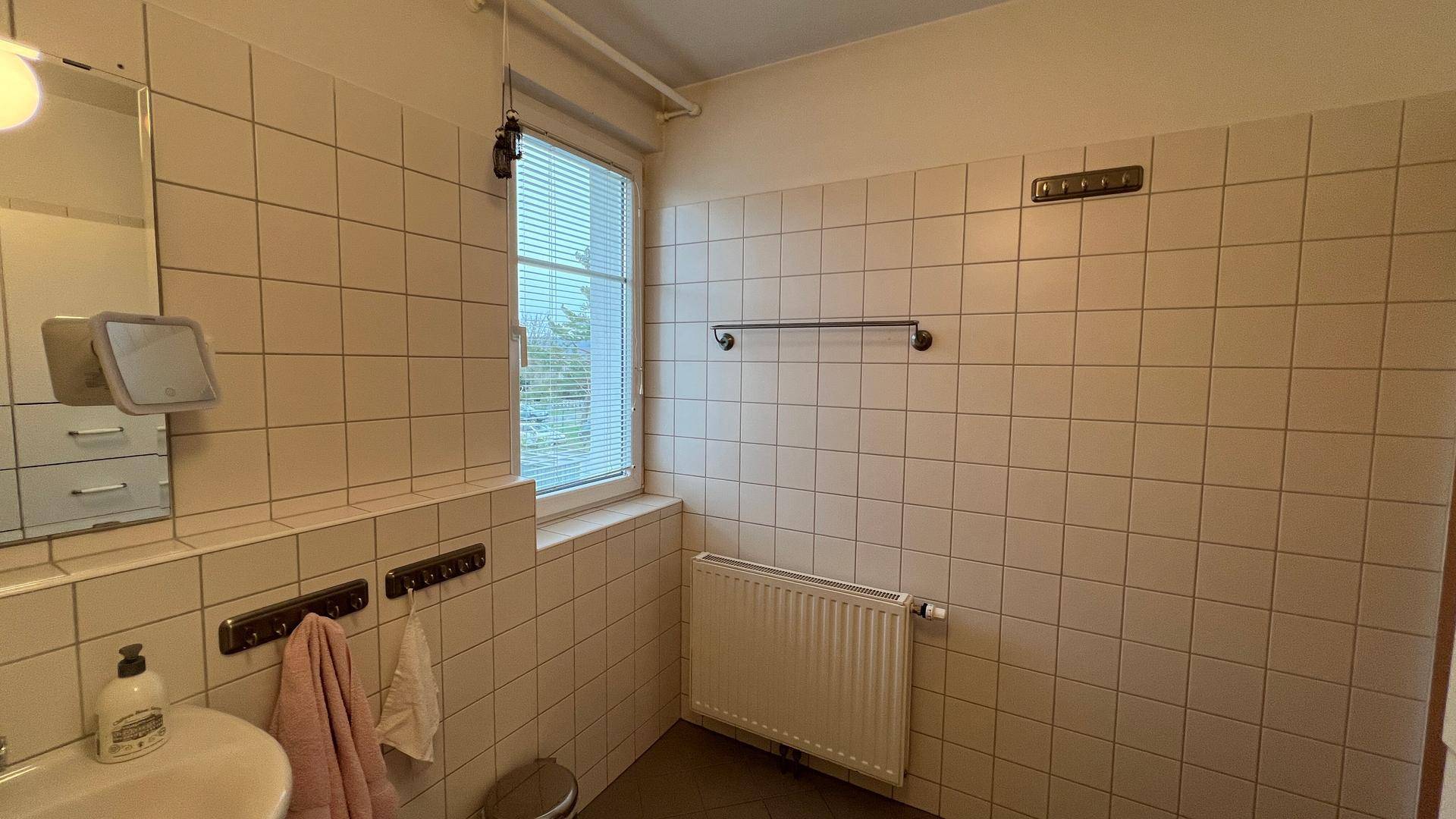 Badezimmer mit Fenster für Tageslicht und Belüftung, ausgestattet mit Heizkörper und Fliesen.