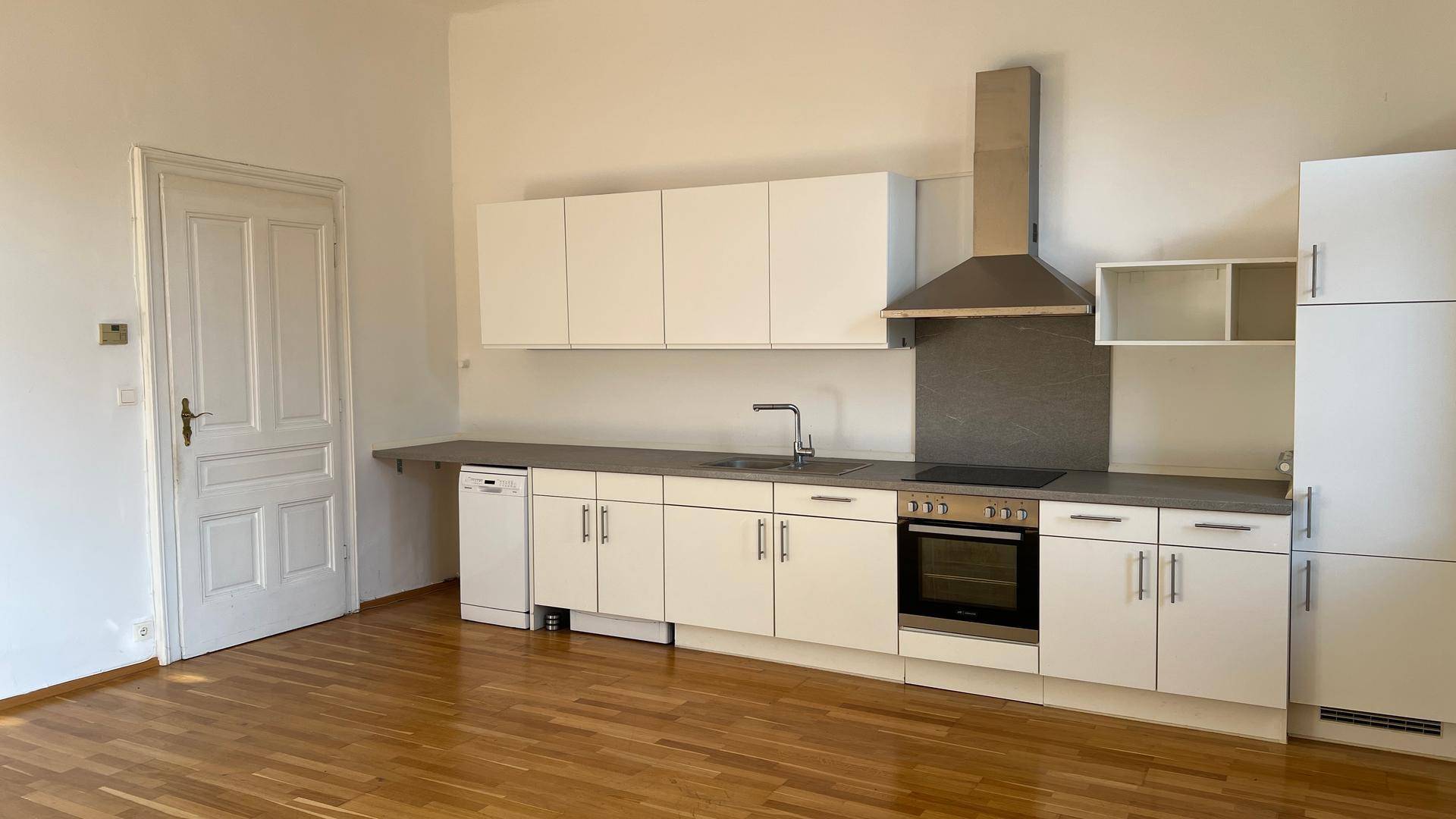 Moderne Einbauküche mit weißen Schränken, Holzparkettboden und integrierten Geräten.