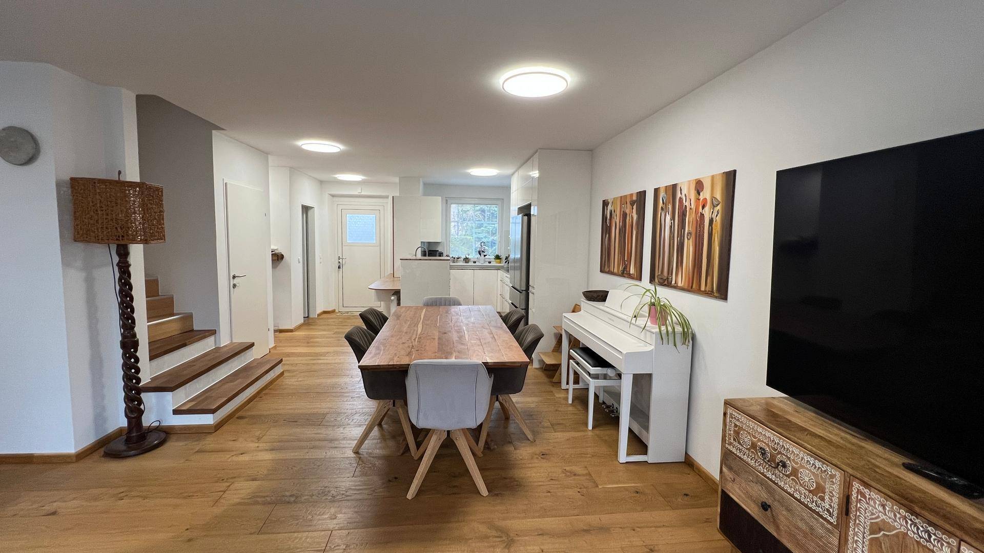 Geräumiger Wohn- und Essbereich mit Holzboden, Klavier und Treppenzugang.