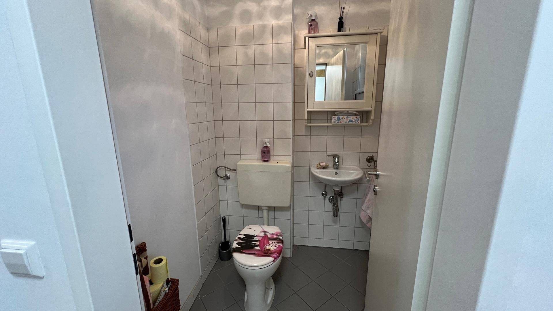Kleines Gäste-WC mit weißen Fliesen, Toilette und Waschbecken, funktional eingerichtet.
