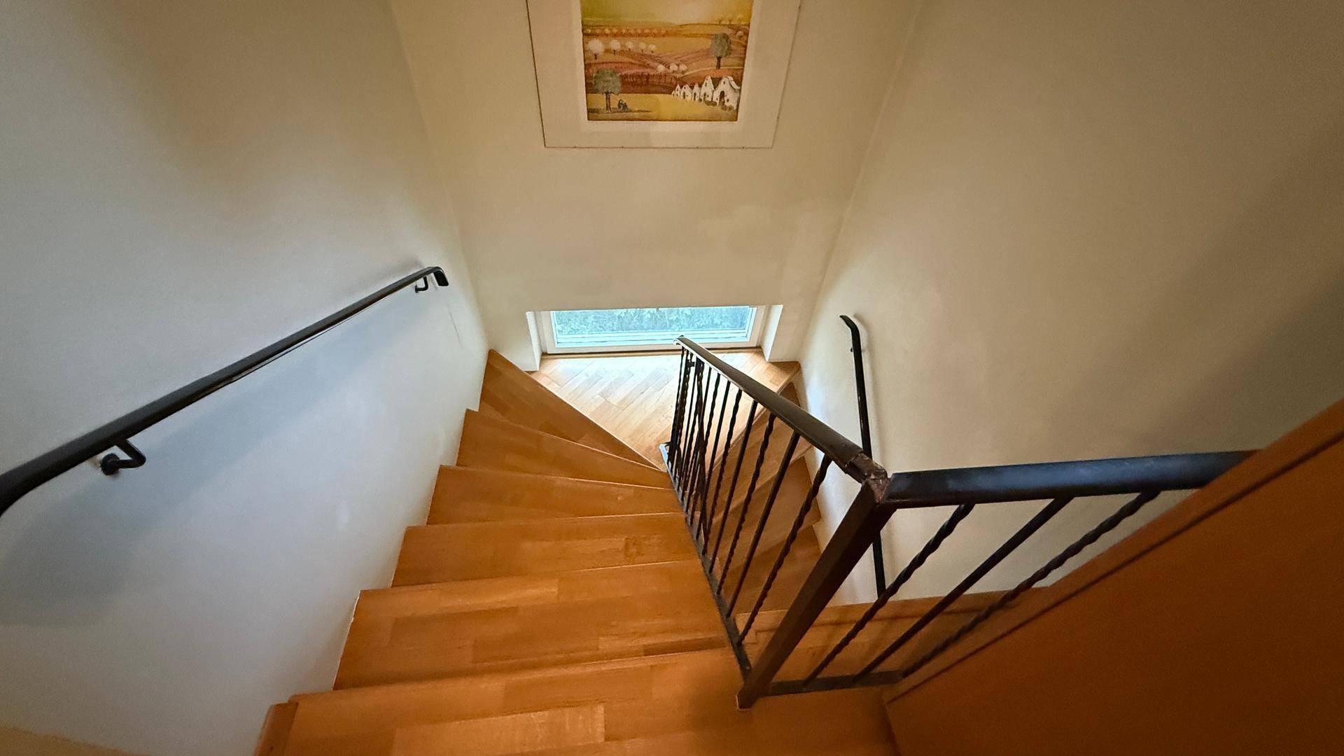 Holztreppe führt in die obere Etage, beleuchtet durch ein Fenster im Treppenhaus.