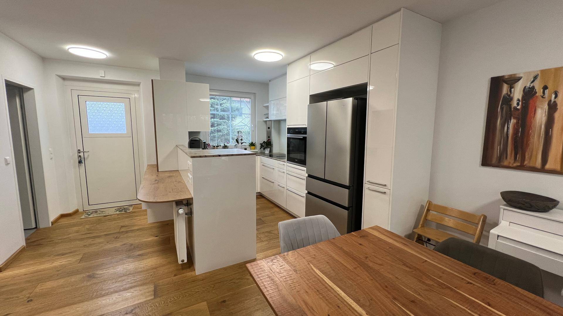 Moderne, offene Küche mit weißen Hochglanzfronten, Holzboden und integrierten Geräten.