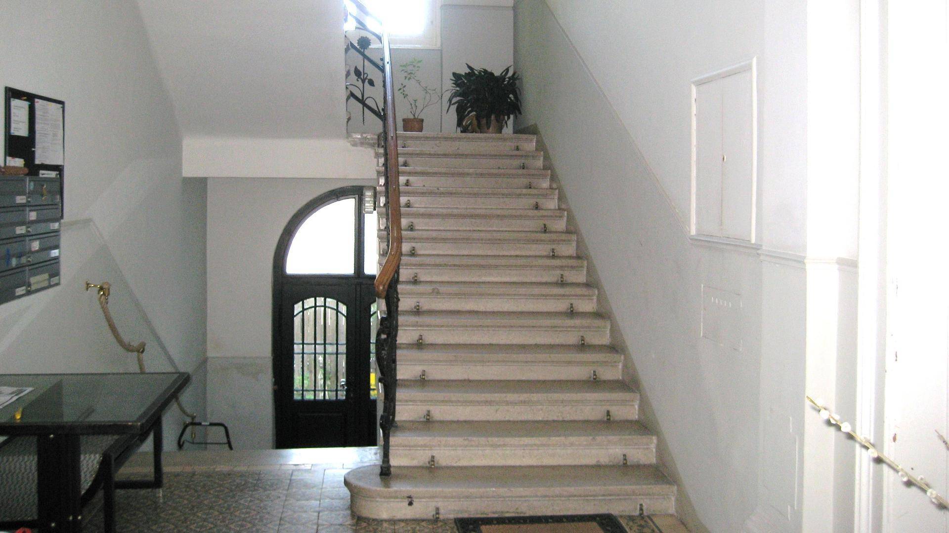 Geräumiger Treppenaufgang in einem Altbau mit Marmorstufen und einem historischen Eingangsbereich.