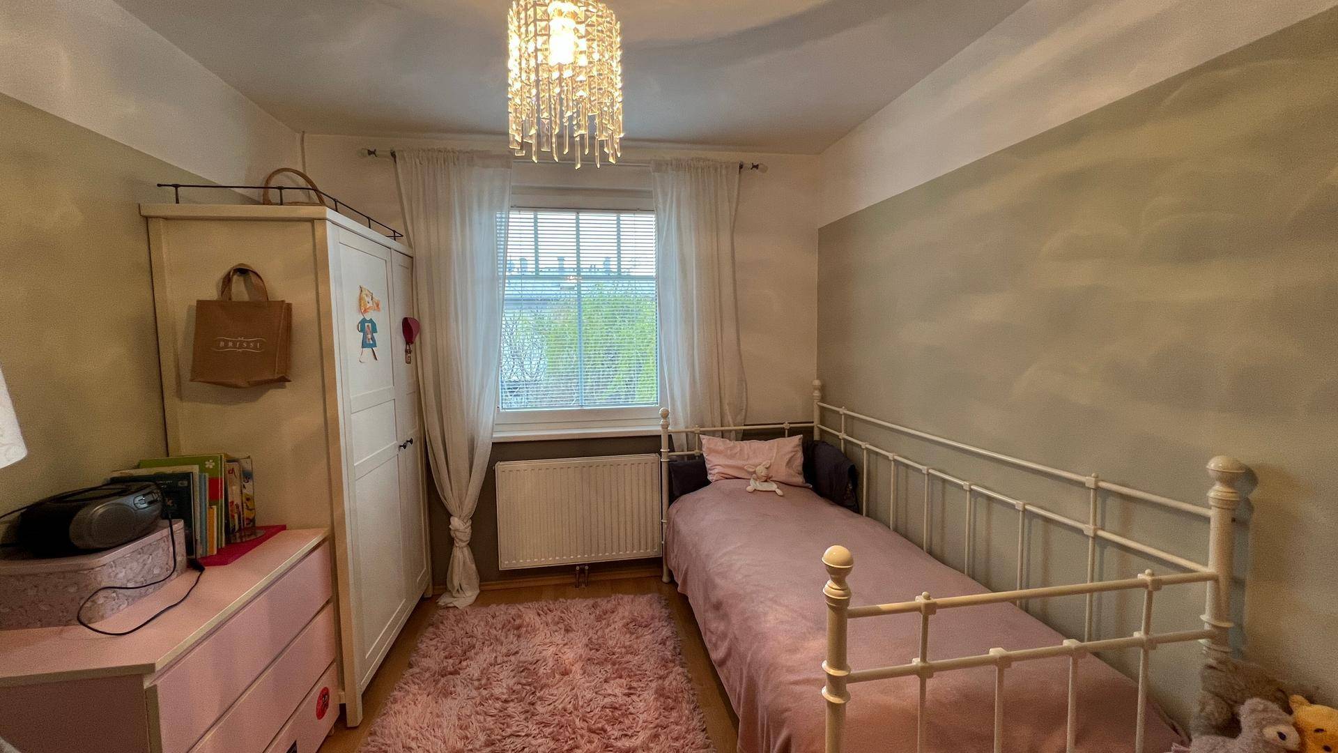 Gemütliches Kinderzimmer mit Einzelbett, rosa Teppich und Fenster für viel Tageslicht.