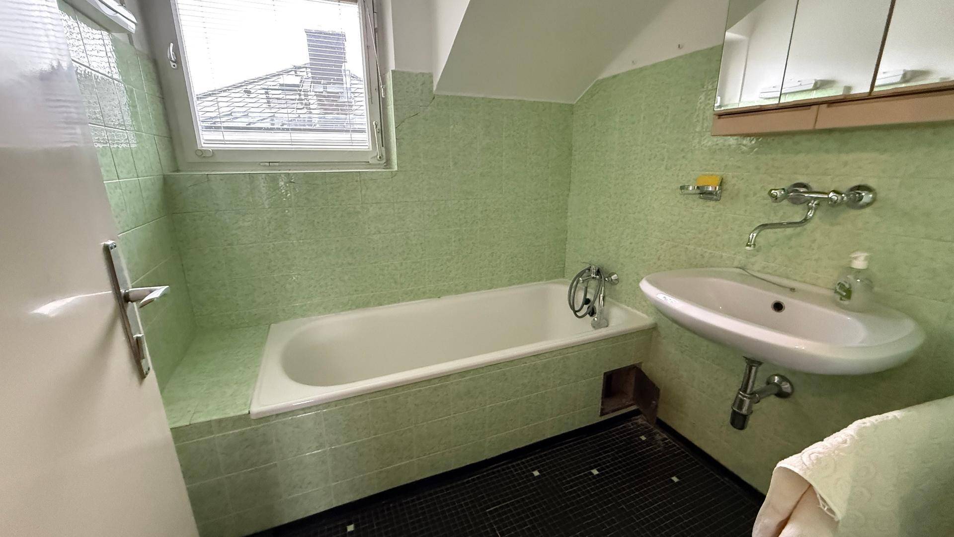 Badezimmer mit grünen Fliesen, Badewanne und Waschbecken, im Stil der 80er Jahre.