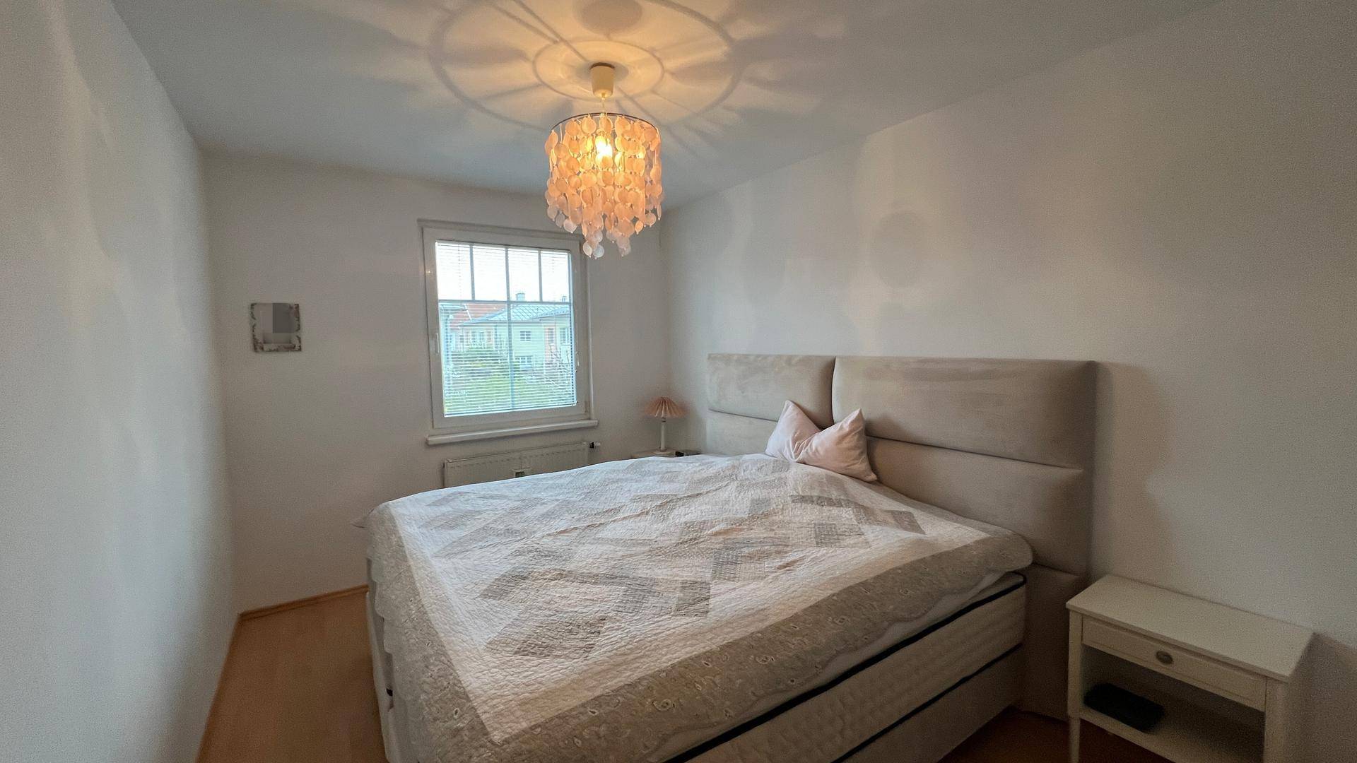 Schlafzimmer mit Doppelbett, Nachttisch und hellem Laminatboden, schlicht und funktional.