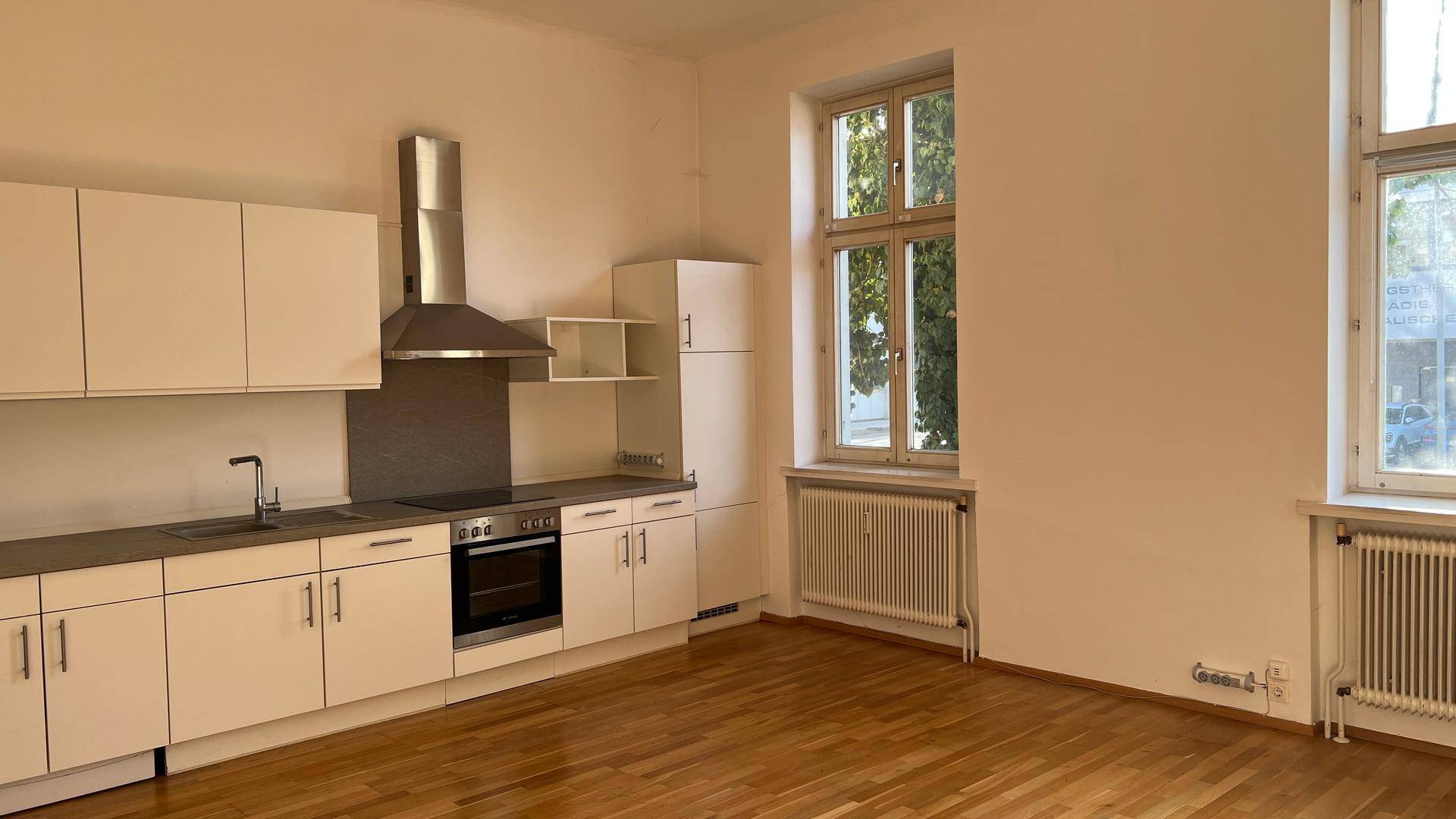 Helle Küche mit weißen Schränken, Holzparkett und großen Fenstern, die viel Tageslicht hereinlassen.
