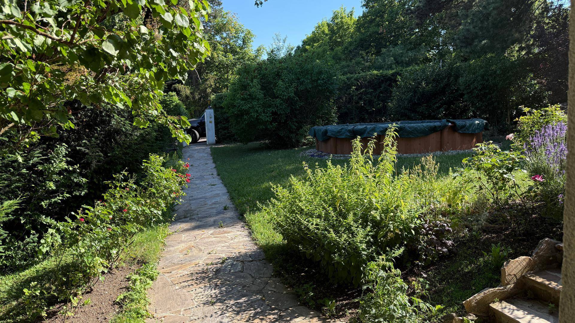 Steinplattenweg führt durch den grünen Garten zu einem abgedeckten Poolbereich.