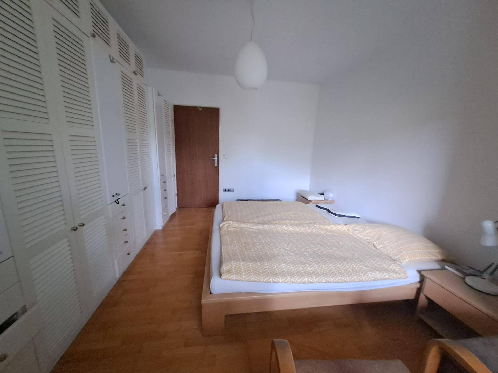 Gemütliches Schlafzimmer mit Holzboden und einer langen Reihe weißer Schranktüren für viel Stauraum.