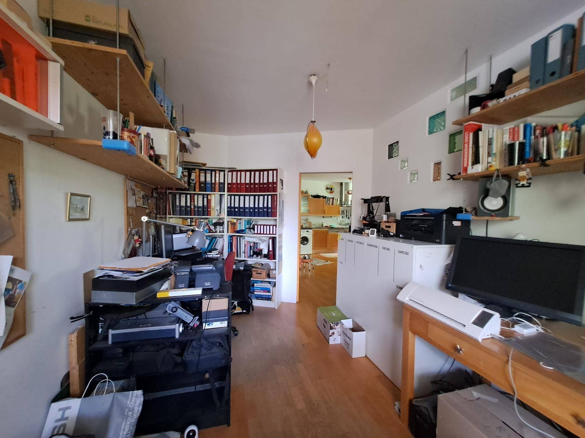 Gut organisiertes Arbeitszimmer mit umfangreichen Regalen und Blick in den angrenzenden Wohnbereich.