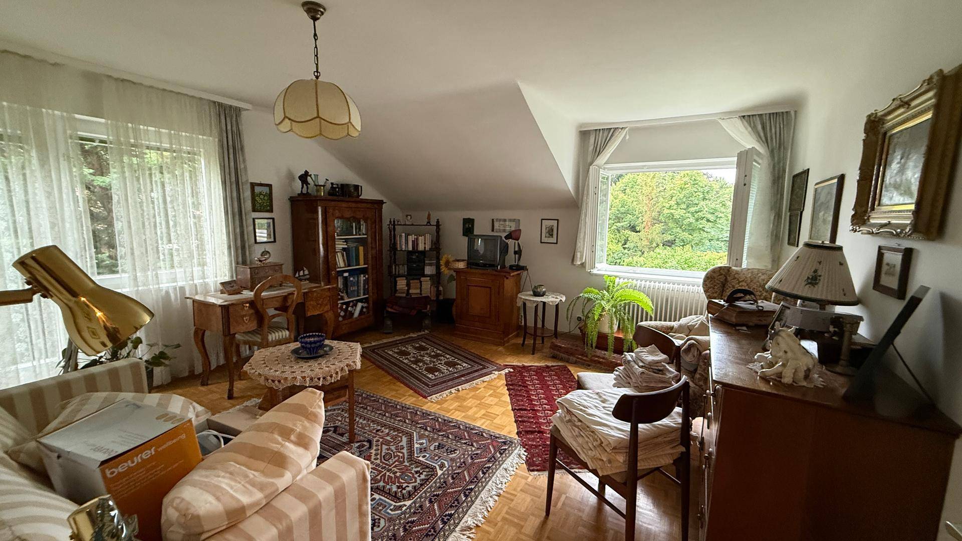 Dachgeschoss-Wohnzimmer mit schrägen Wänden, Parkettboden und Blick ins Grüne.
