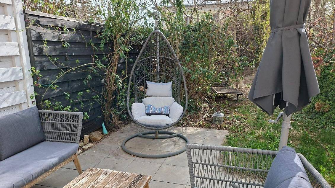 Kleiner, gepflegter Gartenbereich mit Hängesessel und Sitzgelegenheiten, umgeben von Hecken.