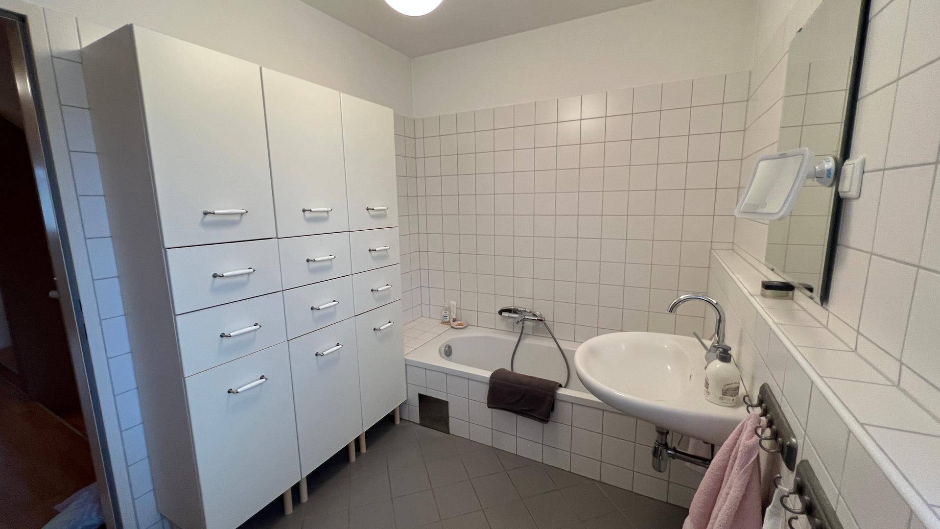 Helles Badezimmer mit Badewanne, Waschbecken und praktischen Einbauschränken für Stauraum.