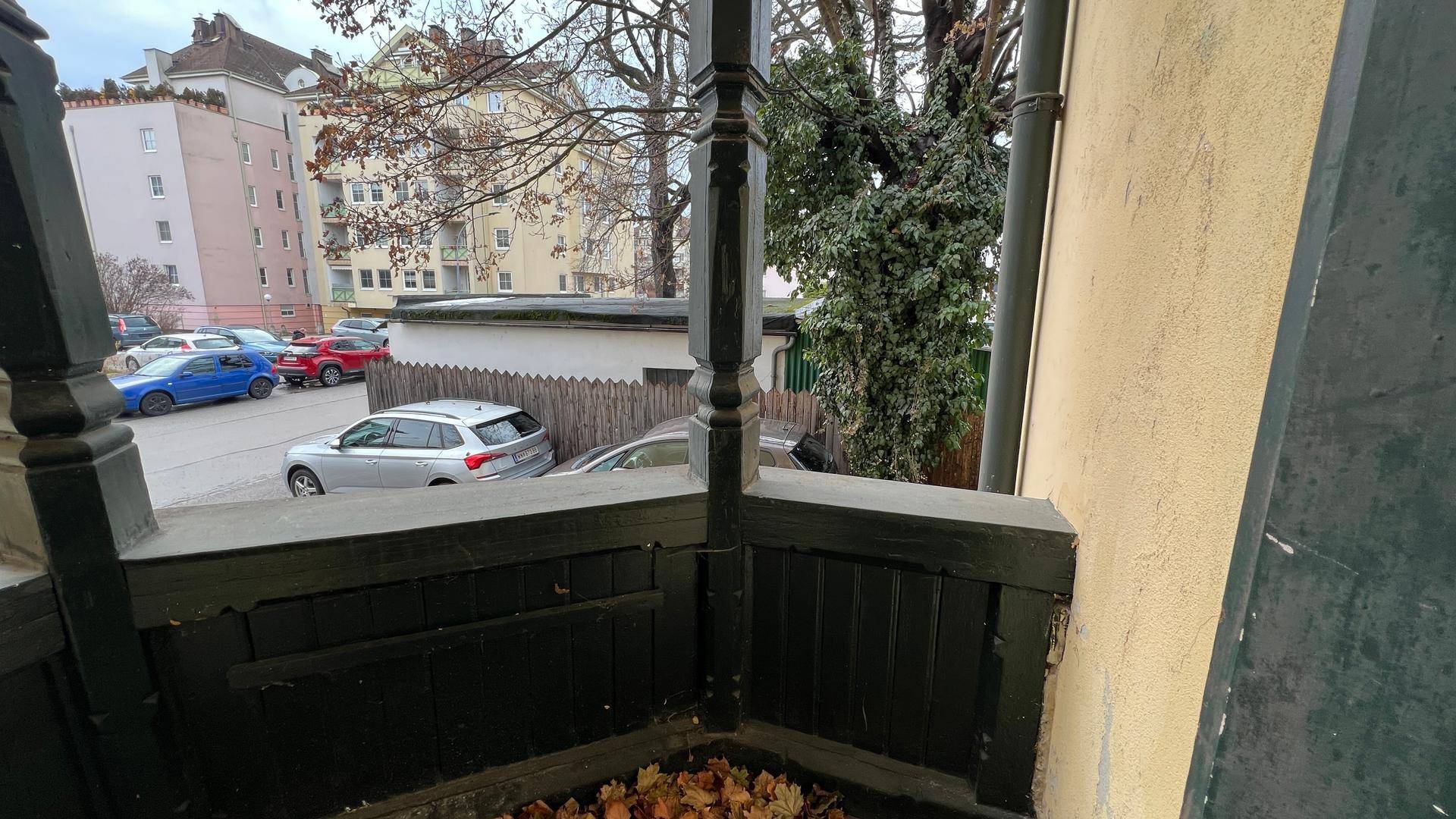 Blick von einem Balkon auf die umliegende Stadtlandschaft mit parkenden Autos und Gebäuden.