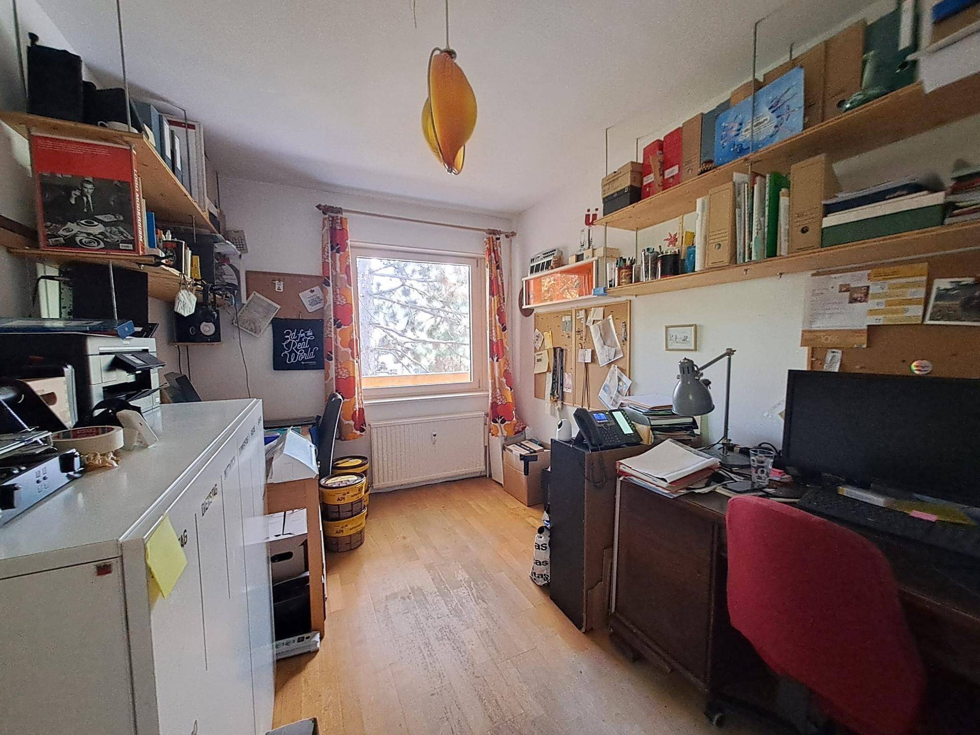 Helles Arbeitszimmer mit Schreibtisch, Regalen und Fenster, ideal für Home-Office-Tätigkeiten.