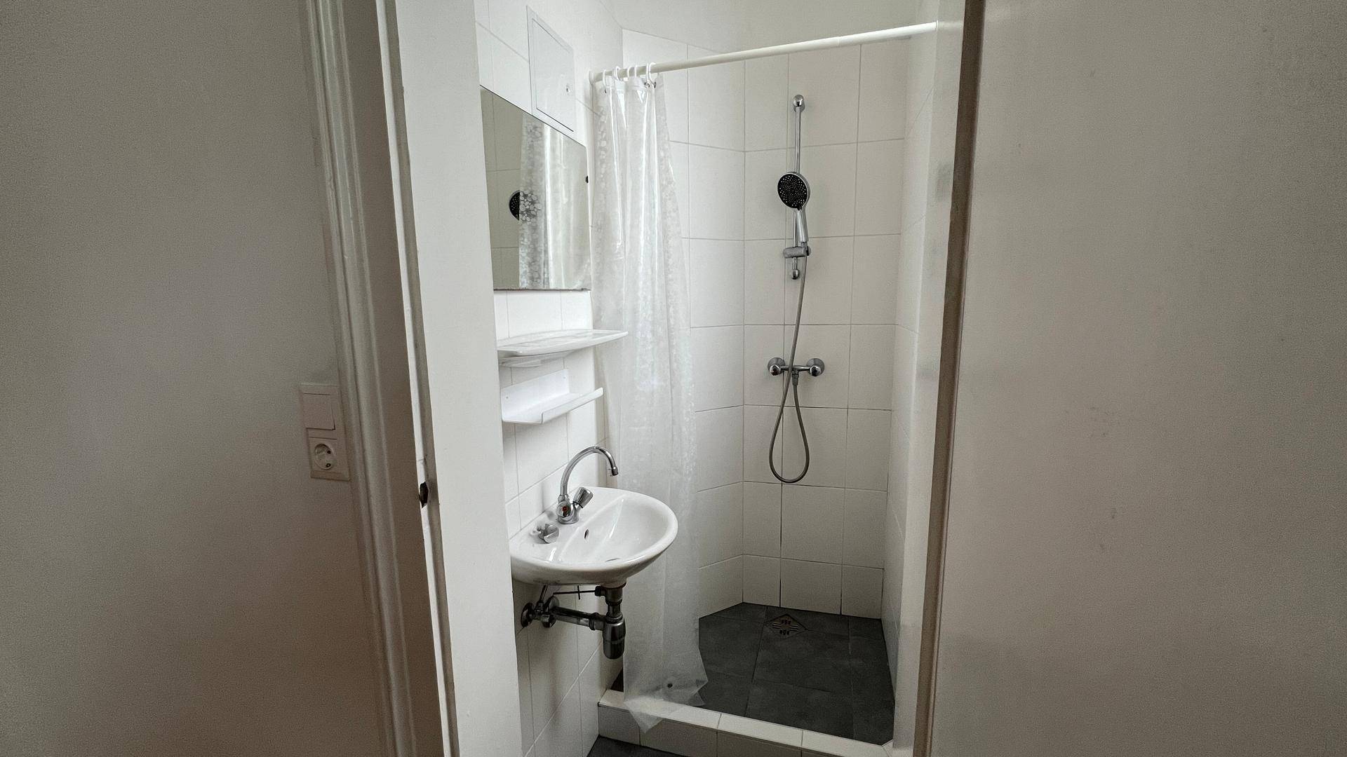 Kleines Badezimmer mit Dusche, Waschbecken und weiß gefliesten Wänden in funktionalem Design.