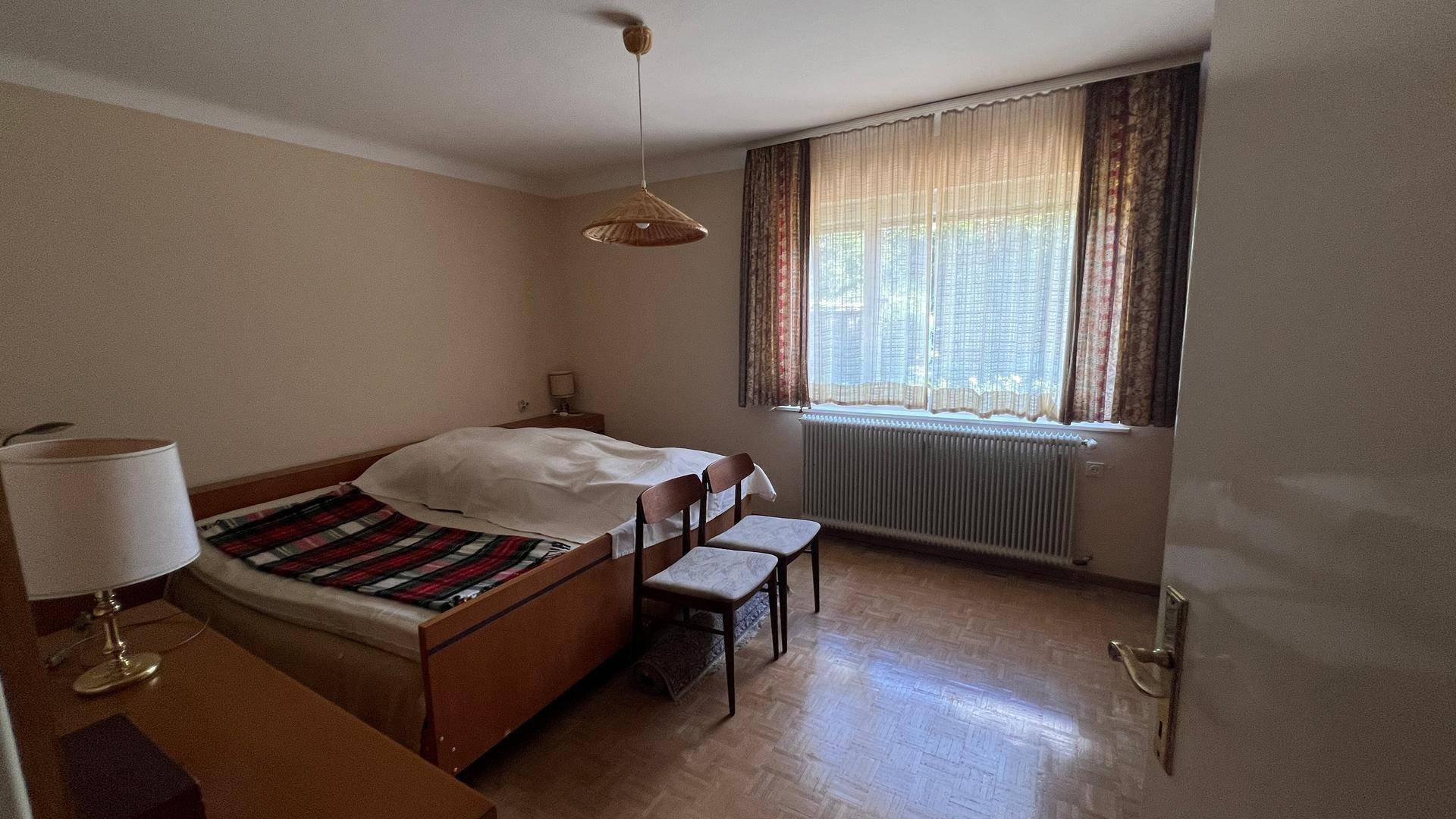 Gemütliches Schlafzimmer mit Parkettboden, großem Fenster und traditionellen Vorhängen.