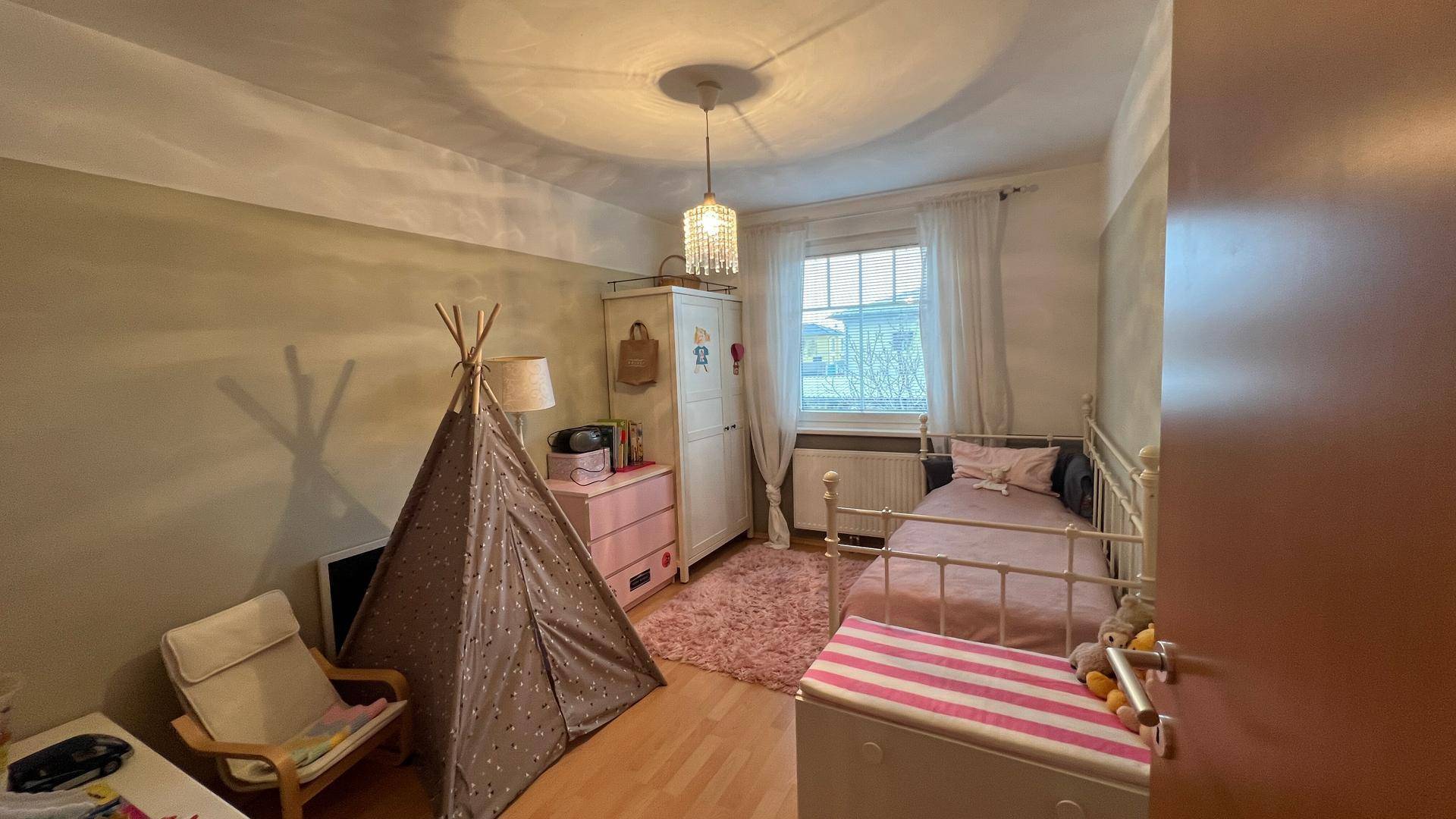 Kinderzimmer mit Einzelbett, Spielzelt und hellem Laminatboden, gemütlich eingerichtet.
