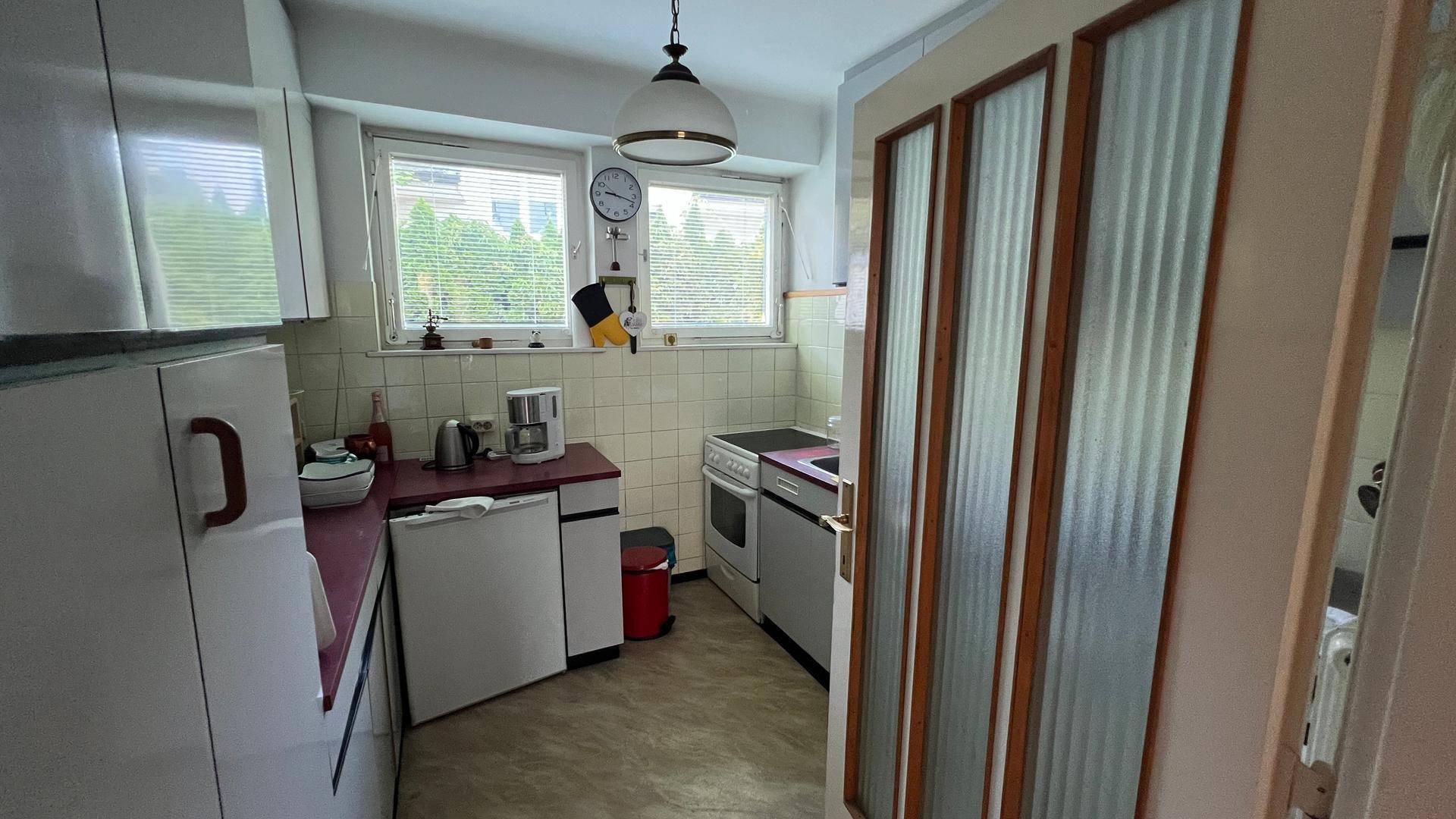 Funktionale Küche mit weißen Schränken, Elektroherd und Fenster mit Jalousien.