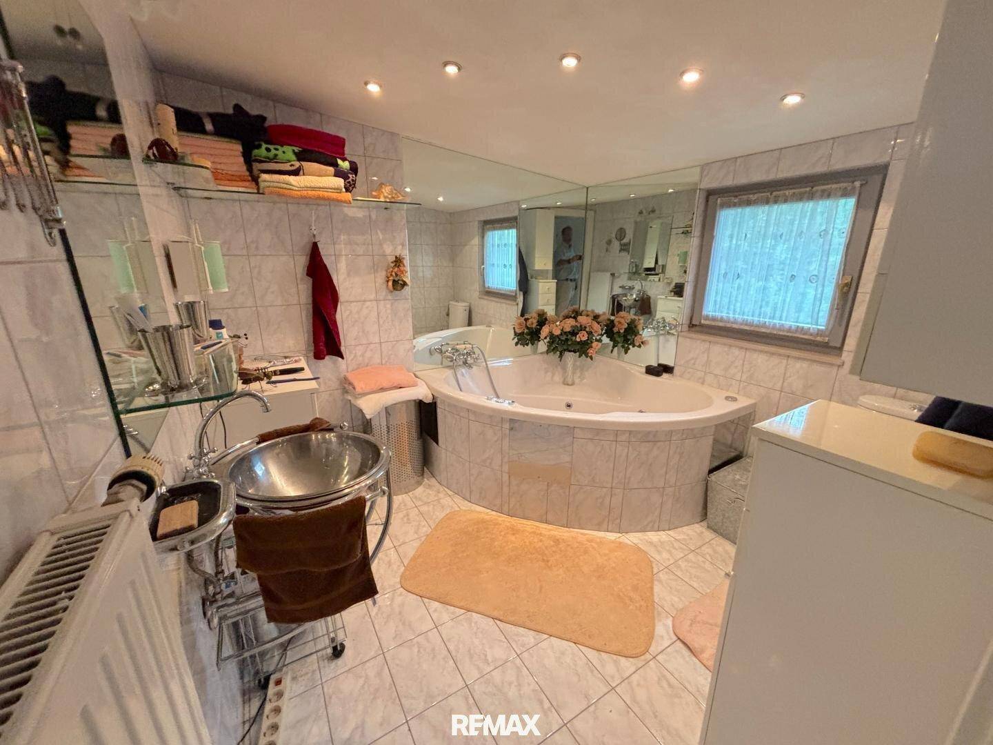 Badezimmer mit großer Eckbadewanne, gefliesten Wänden und einem breiten Spiegel.
