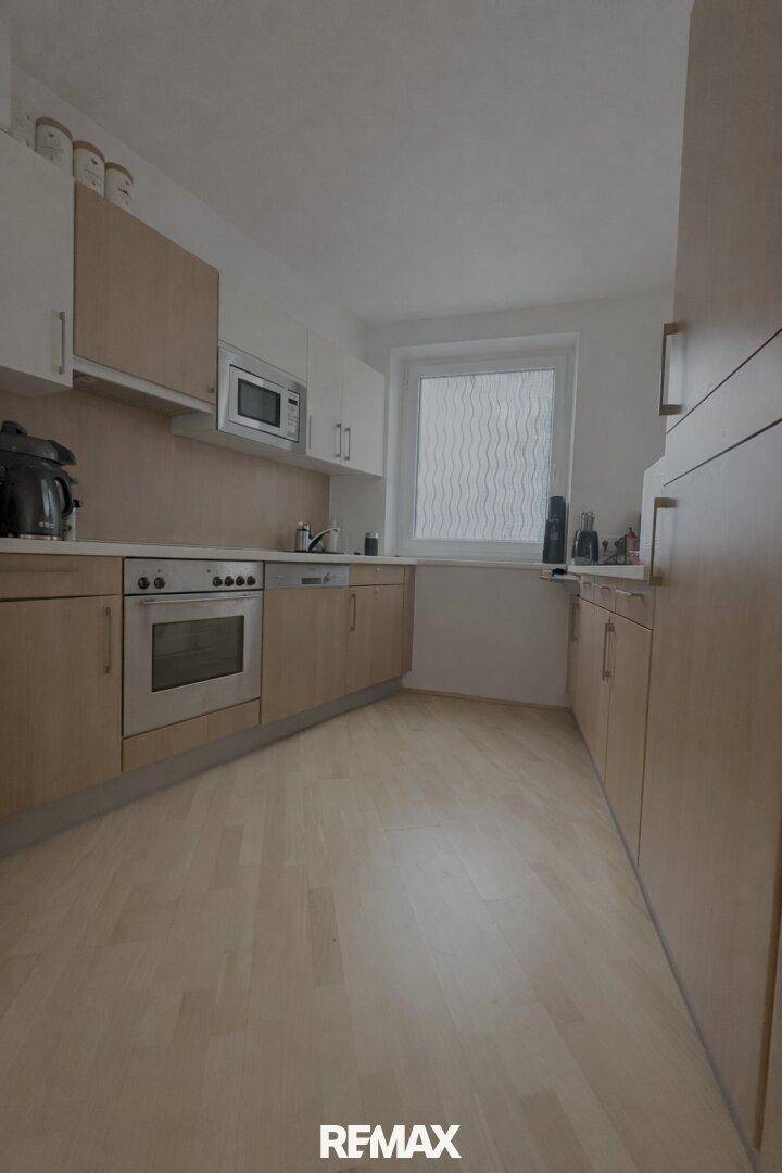 Funktionale Küche mit hellen Holzschränken, Einbaugeräten und Fenster.