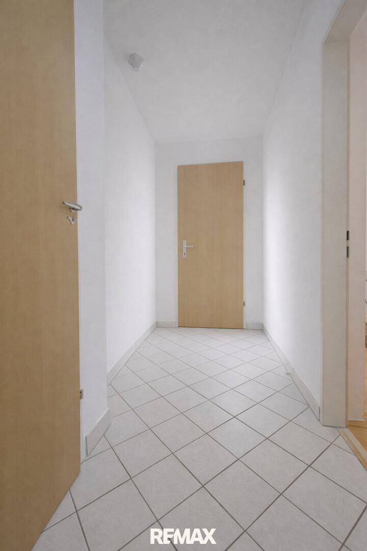 Heller Flur mit diagonal verlegten Fliesen und Holztür.