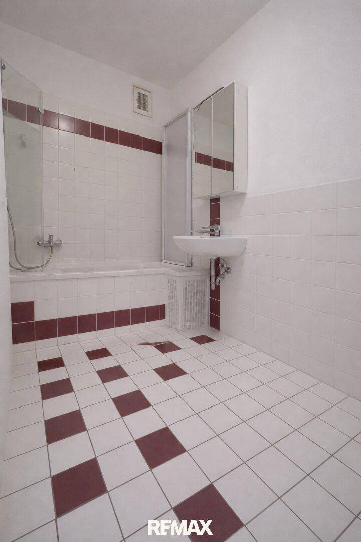 Badezimmer mit Badewanne, Waschbecken und rot-weißen Fliesen.