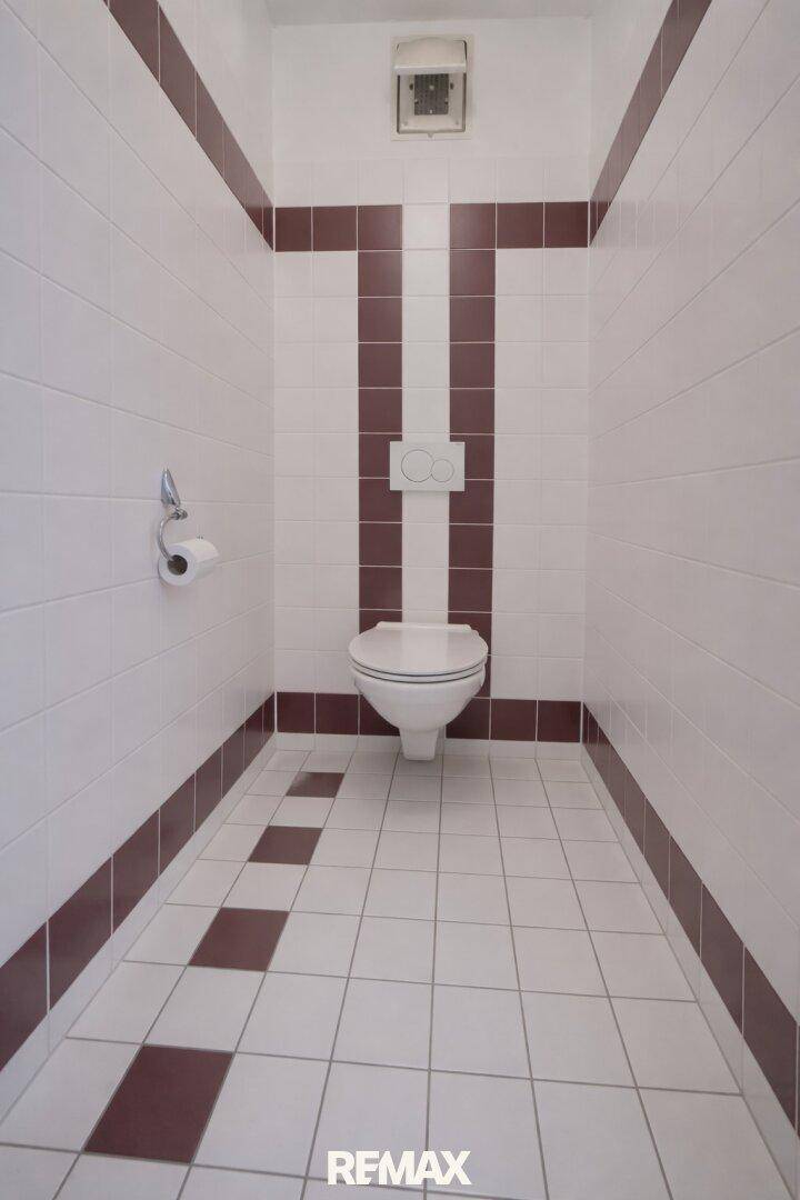 Separates WC mit Wand-WC und rot-weißen Fliesen.