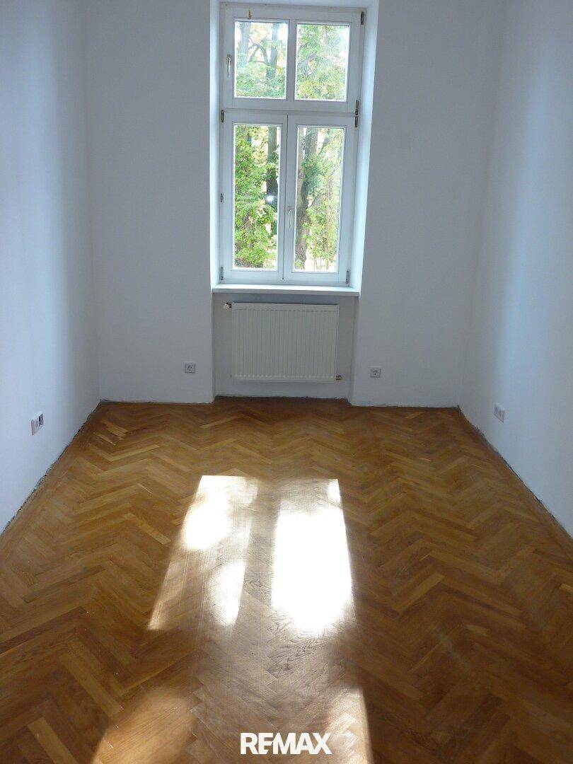 Sonniger Raum mit elegantem Fischgrätparkett und einem großen Fenster, das den Blick nach draußen freigibt.