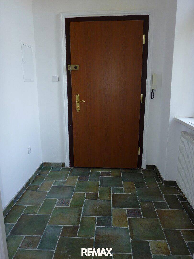 Eingangsbereich mit einer robusten Holztür und einem Boden aus grün-grauen Fliesen.