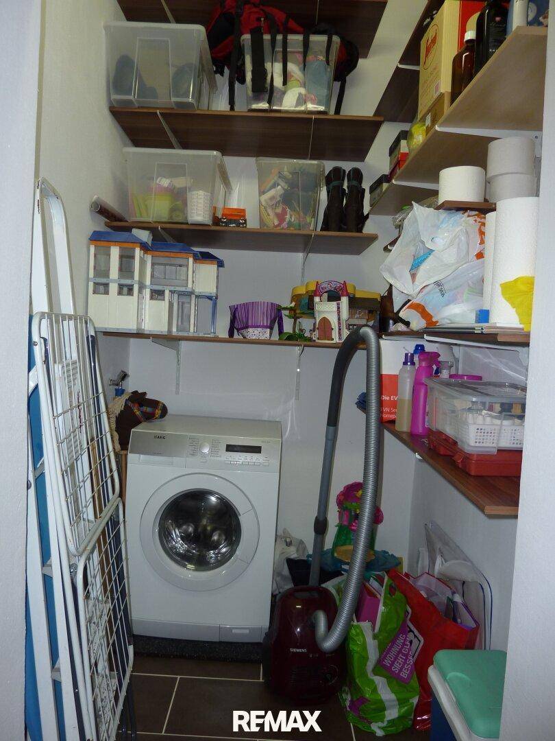 Praktischer Hauswirtschaftsraum mit Waschmaschine, Regalen und Stauraum für Haushaltsgeräte.