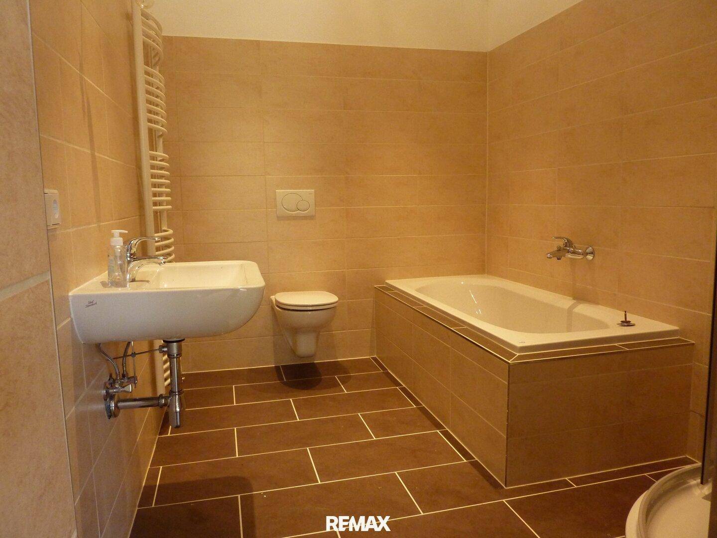 Modernes Badezimmer mit beigefarbenen Wandfliesen, dunklem Boden und einer Badewanne sowie Waschtisch.