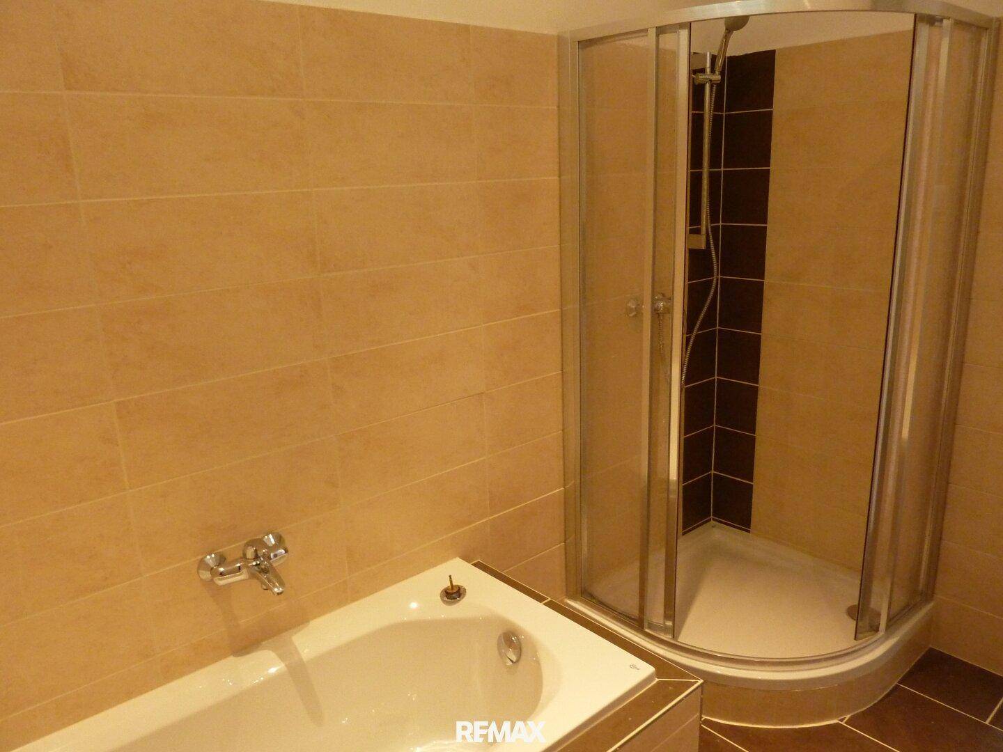 Badezimmer mit Badewanne und einer praktischen Eckduschkabine, ausgestattet mit beigefarbenen Fliesen.