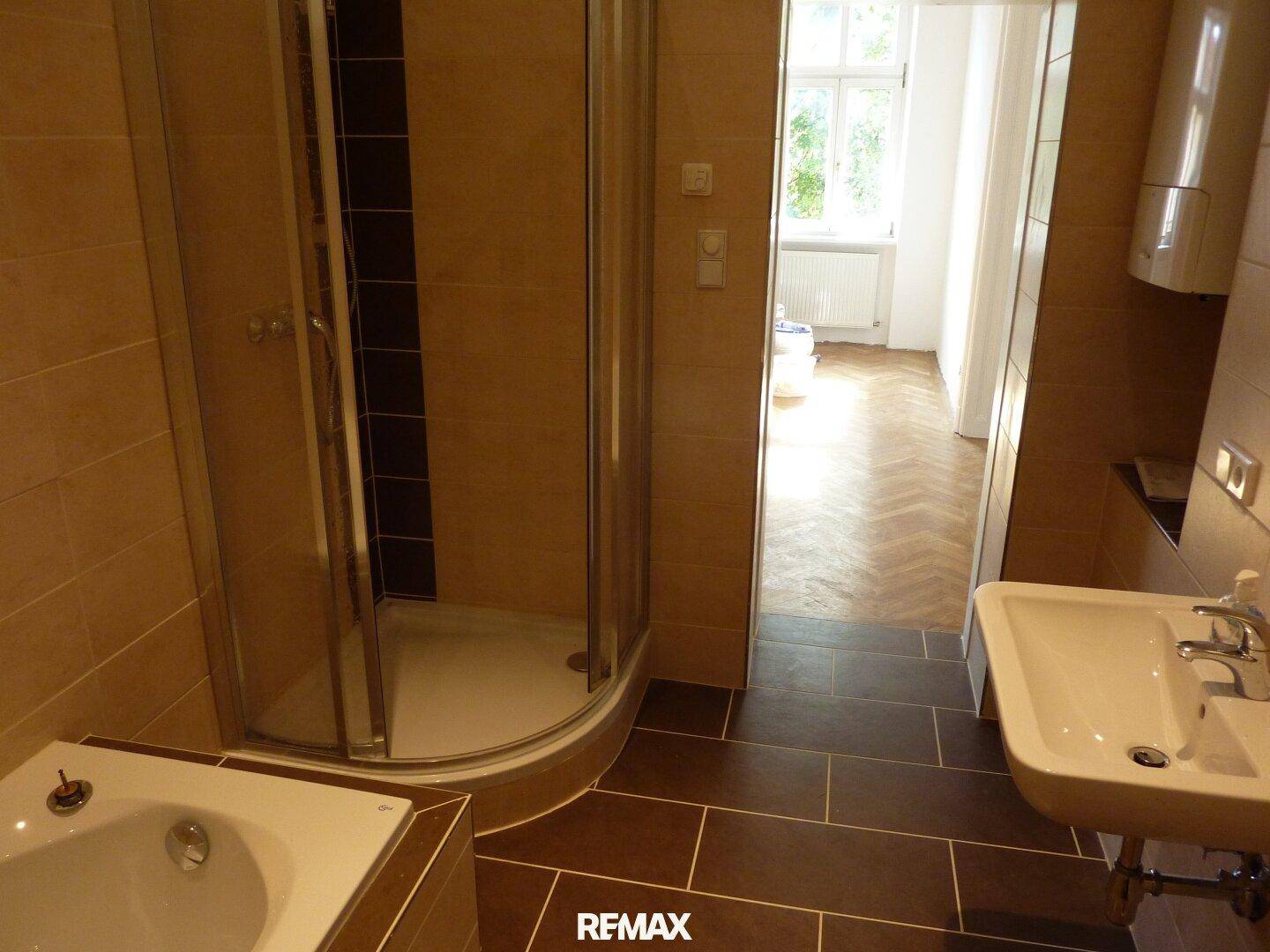 Badezimmer mit Duschkabine, Waschbecken und kleiner Badewanne, gefliest in warmen Brauntönen.