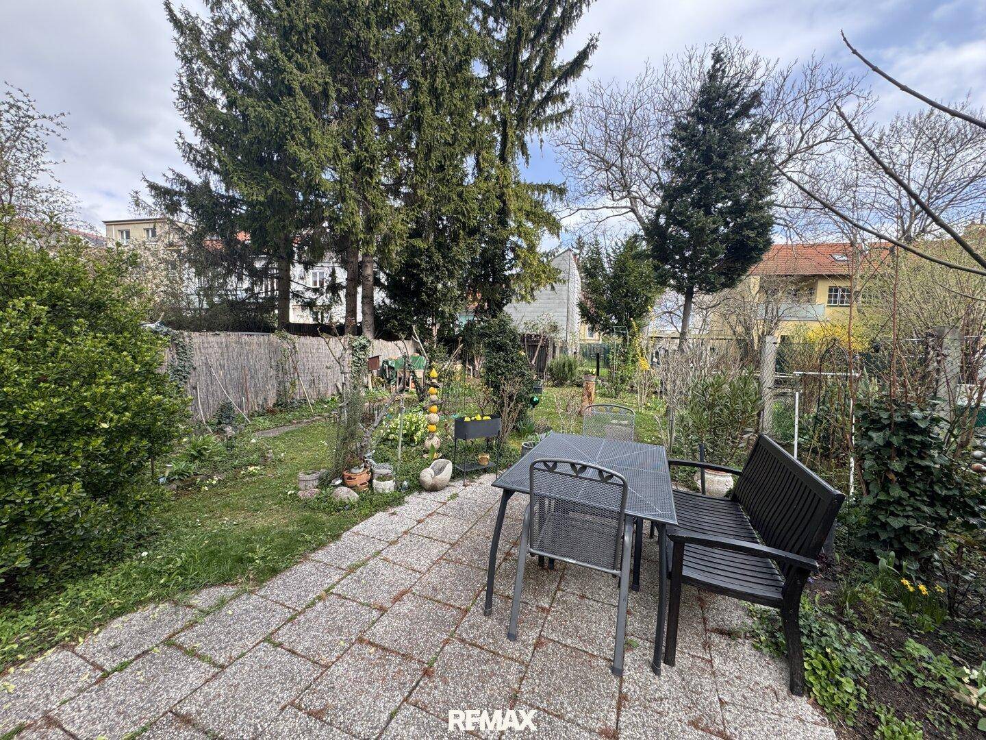 Gemütliche Terrasse mit Sitzgelegenheiten und Blick in den grünen Garten mit hohen Bäumen.