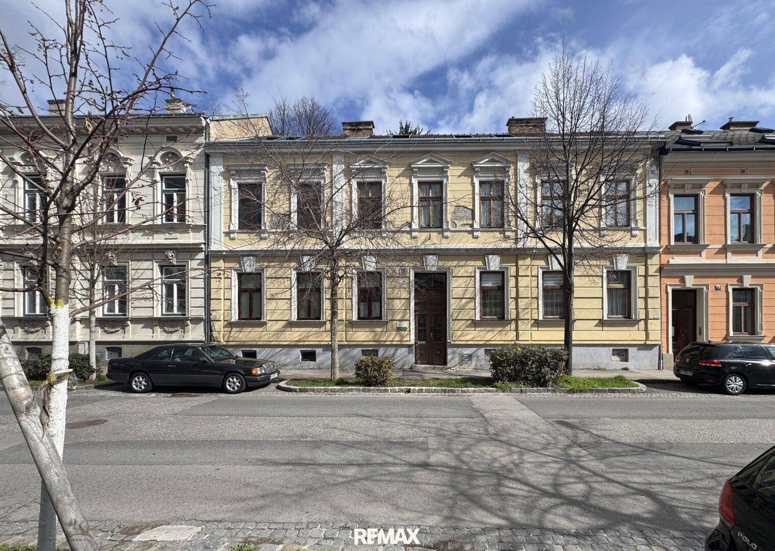 Historische Fassade eines Mehrfamilienhauses in einer städtischen Umgebung mit Bäumen.