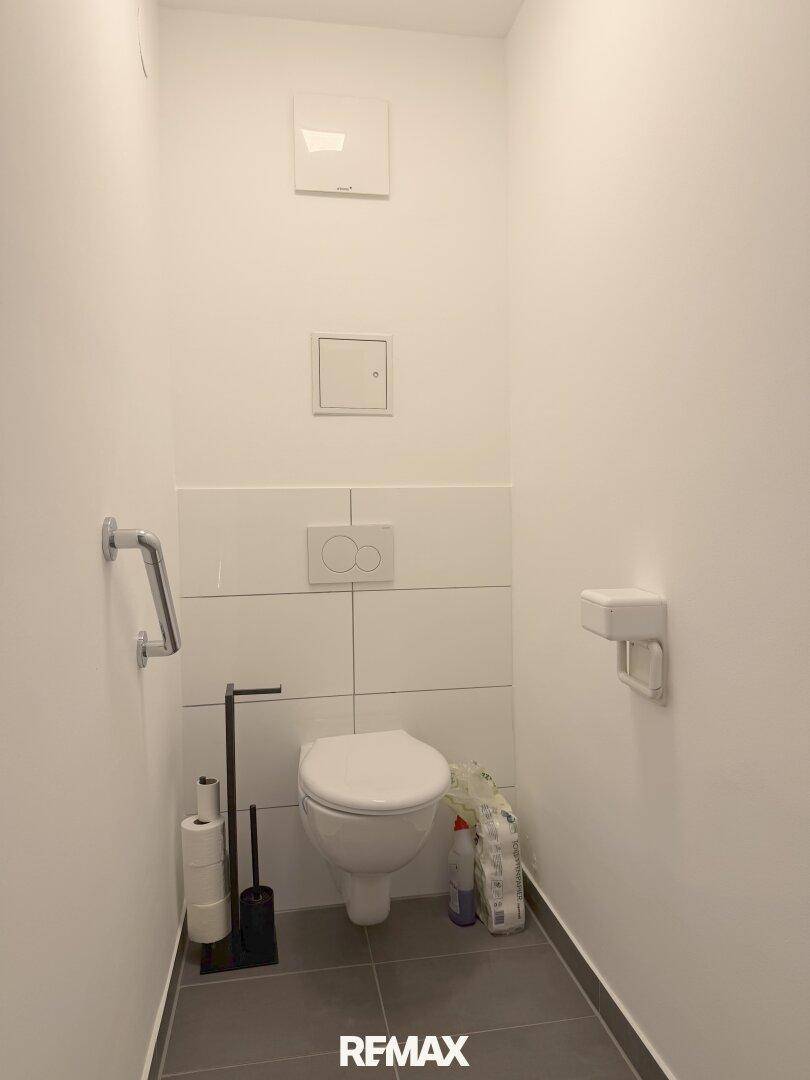 Helles Gäste-WC mit wandhängendem WC und Haltegriff.
