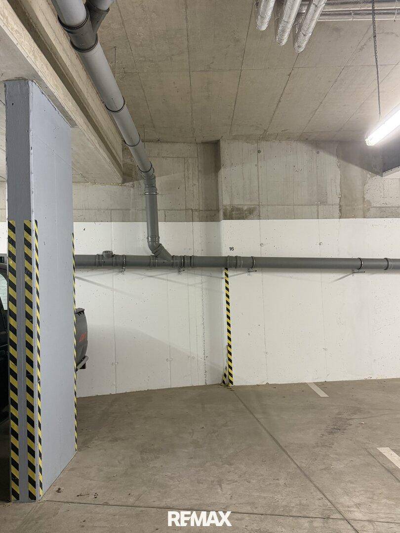 Tiefgarage mit Betonwänden, sichtbaren Rohren und markierten Parkplätzen.