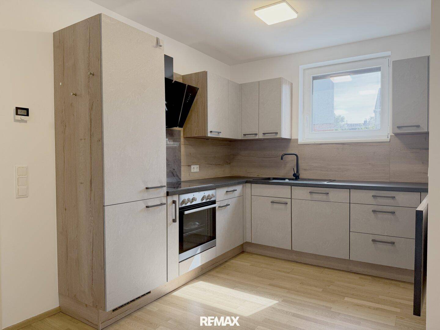 Moderne Einbauküche in hellen Holztönen mit integrierten Geräten und Fenster.