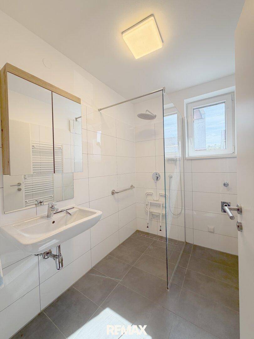 Modernes Badezimmer mit ebenerdiger Dusche, Fenster und Handtuchheizkörper.