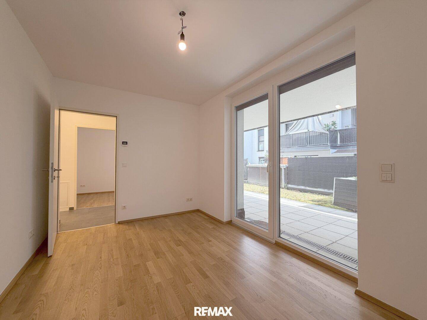 Geräumiges, helles Zimmer mit Holzboden und großen Fenstern mit Blick auf die Terrasse.