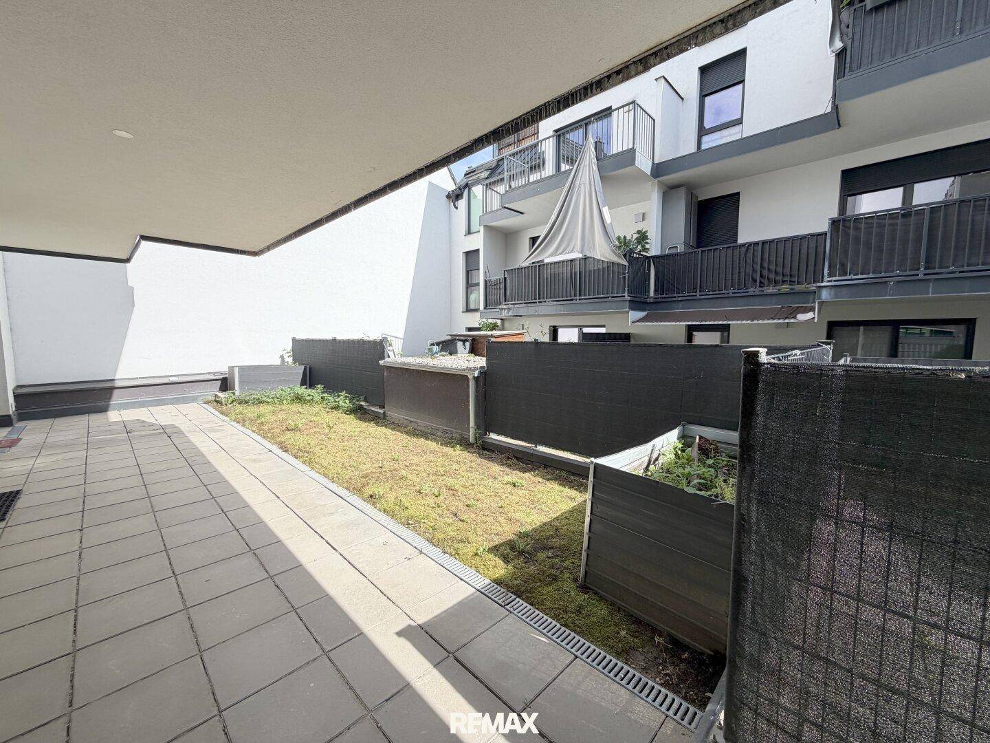 Gepflasterte Terrasse mit kleinem Grünstreifen und Blick auf die Wohnanlage.