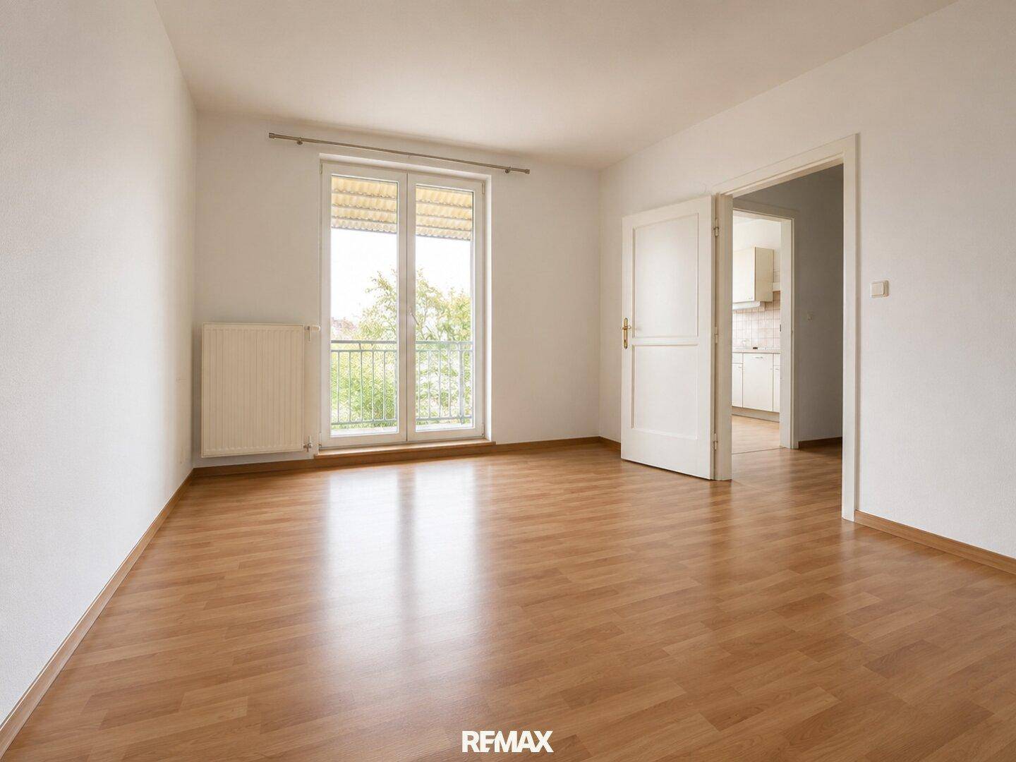 Heller Raum mit Laminatboden, weiß gestrichenen Wänden und Zugang zu einem kleinen Balkon.