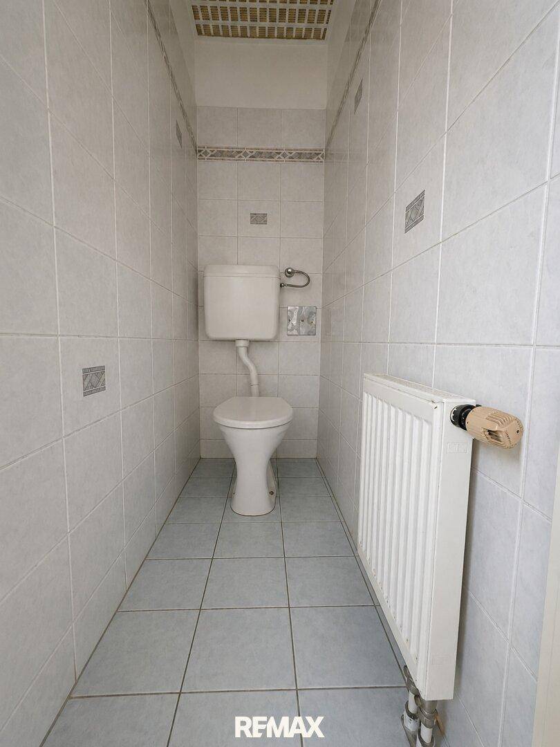 Kleines WC mit hellen Fliesen an Wänden und Boden sowie einem Heizkörper.