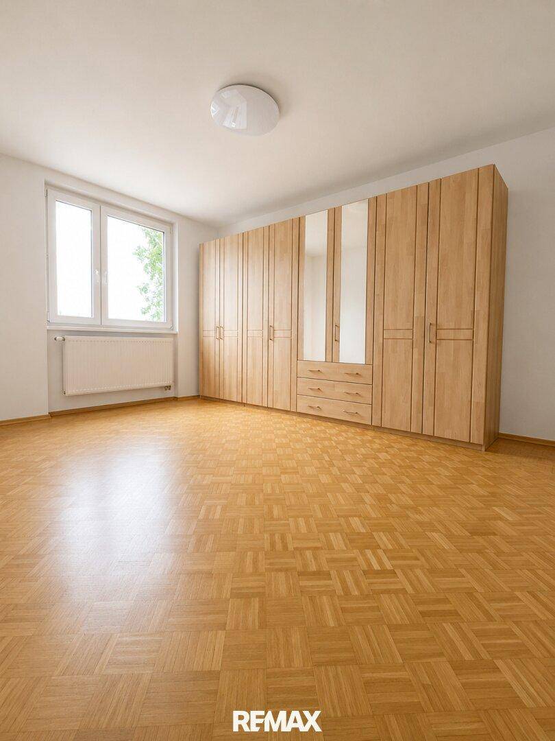 Geräumiges Schlafzimmer mit Parkettboden, großem Fenster und einem Einbauschrank mit Spiegeltüren.