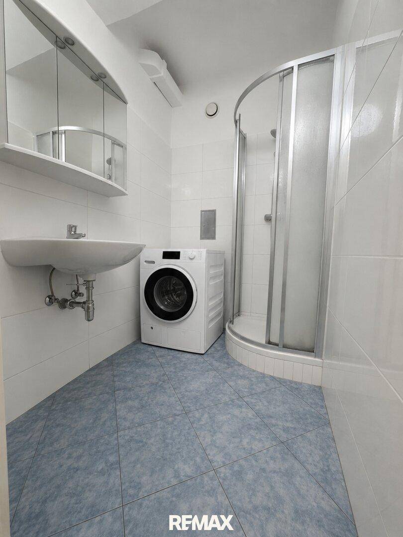 Funktionales Badezimmer mit blauen Bodenfliesen, weißer Wandverkleidung und einer Duschkabine.
