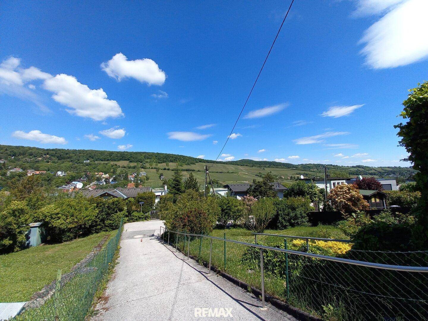 Zufahrtsweg mit Geländer und weitem Blick über die grüne Hügellandschaft an einem sonnigen Tag.