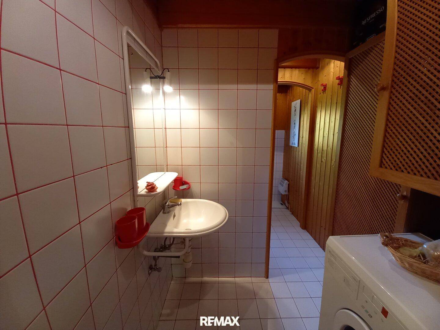 Gefliestes Badezimmer mit Waschbecken und Zugang zu Dusche und WC in hellem Ambiente.