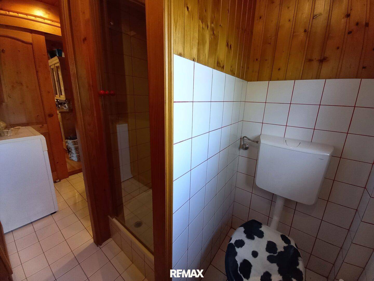 Kleines Badezimmer mit WC, Dusche und weiß-roten Fliesen in funktionalem Design.