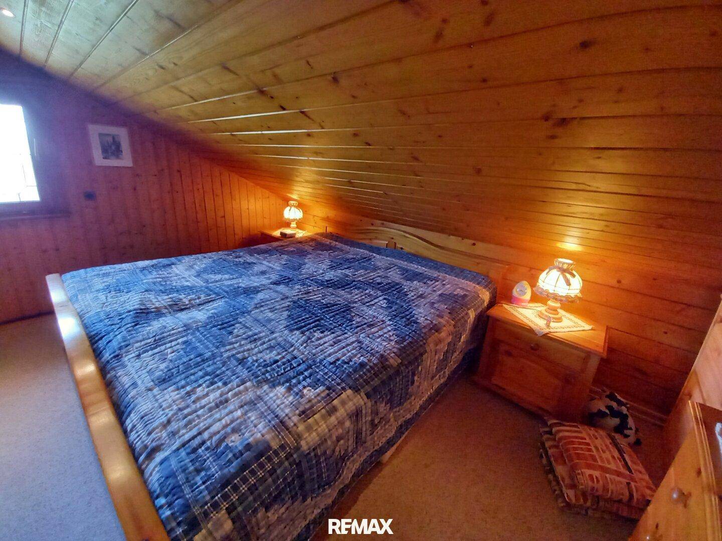 Gemütliches Schlafzimmer im Dachgeschoss mit Holzverkleidung, schrägen Wänden und Doppelbett.